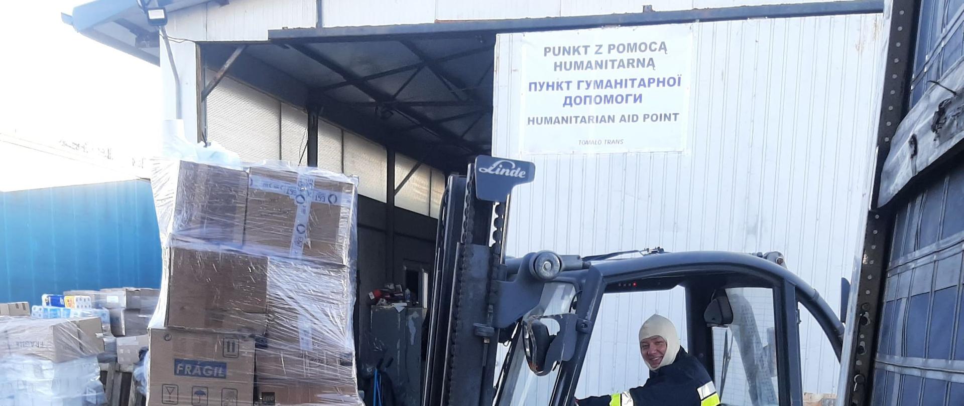 Zdjęcie przedstawia strażaka na wózku widłowym ładującego dary znajdujące się na palecie.