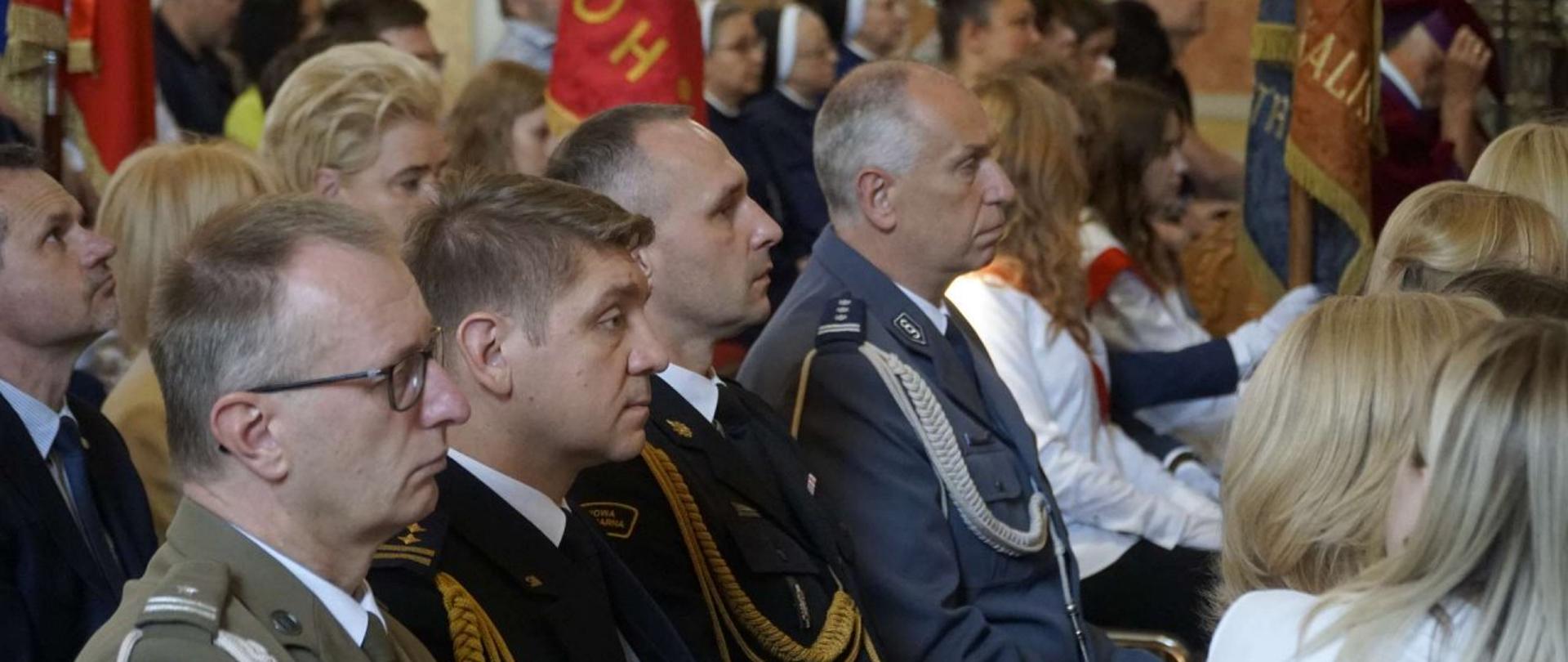 Na zdjęciu widać osoby w Narodowym Sanktuarium Św. Józefa w Kaliszu. Osoby cywilne, funkcjonariusze w umundurowaniu wyjściowym. Pośród osób widać sztandary. Zdjęcie wykonane podczas uroczystości. Światło naturalne, dzienne, Ściany świątyni kolorowe.