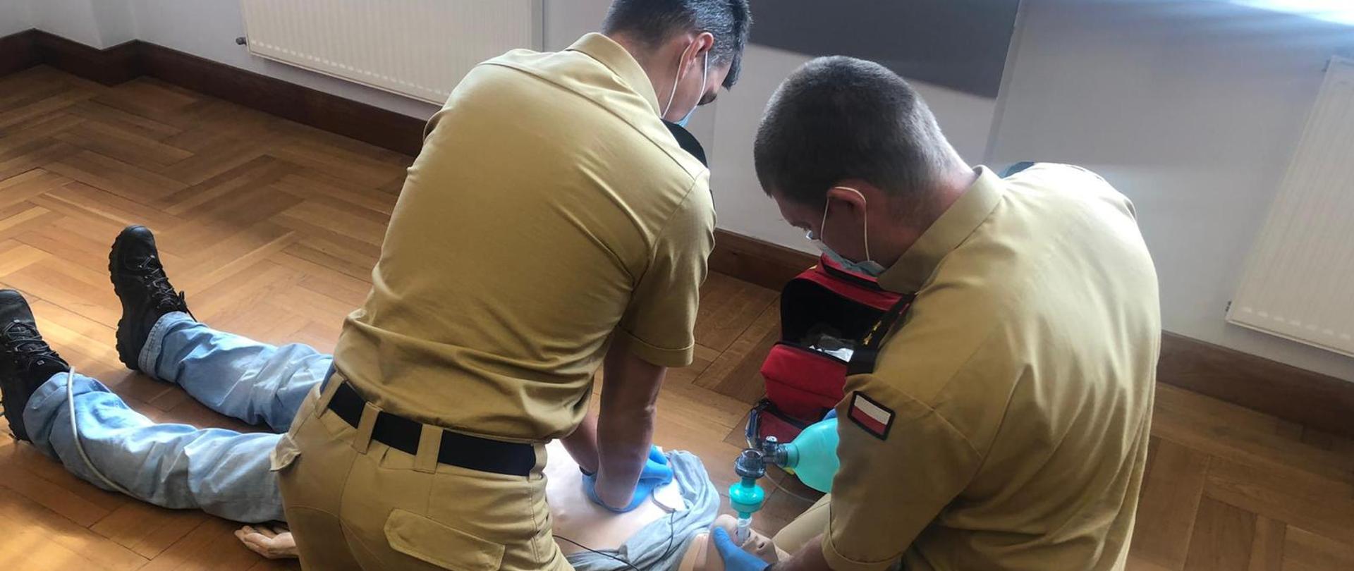 Dwóch strażaków ćwiczy udzielanie pierwszej pomocy na manekinie.
