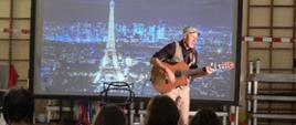 Piosenkarz francuski François Martineau śpiewający i grający na gitarze uczniami na tle widoku z wieżą Eiffela