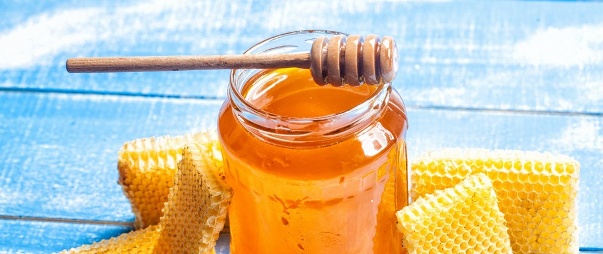 słoik miodu z drewnianą łyżką do miodu i plastrem miodu na błękitnym tle tle
