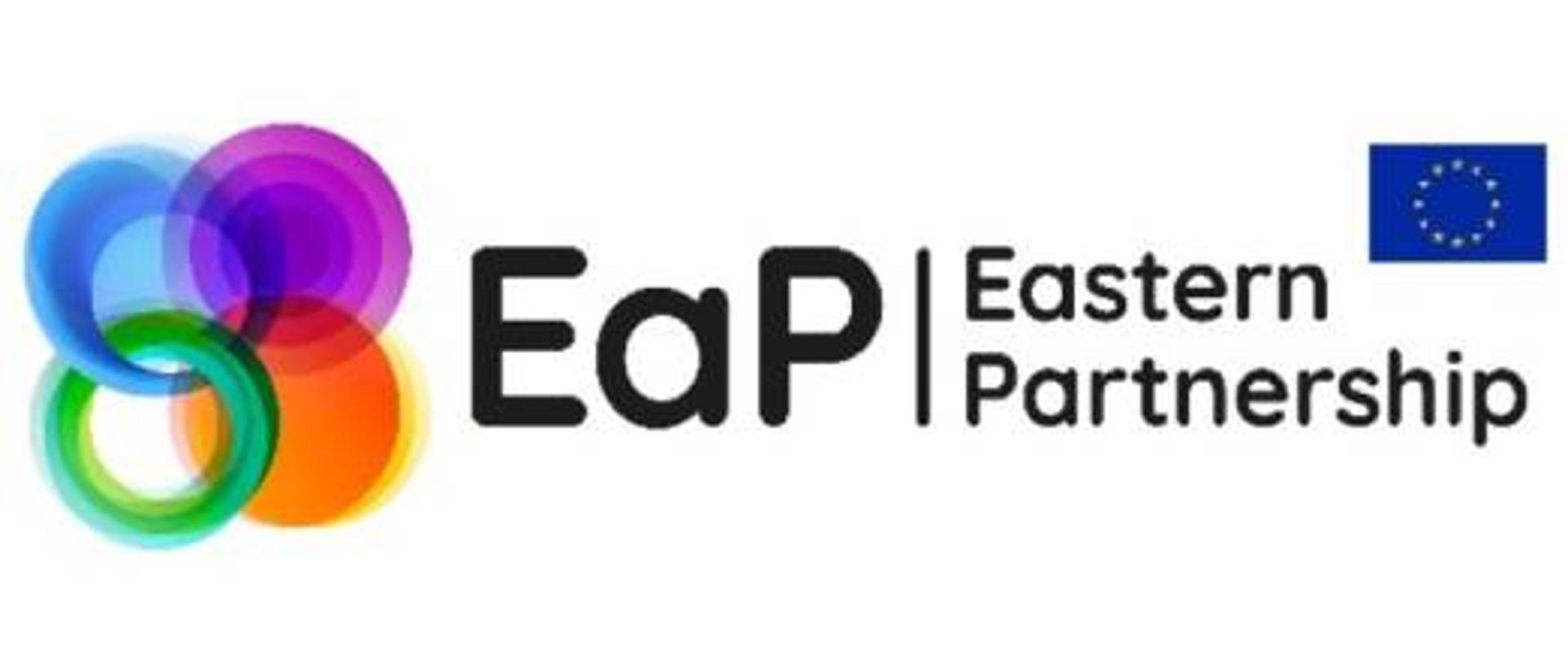 logotyp Partnerstwa Wschodniego: pośrodku skrót EaP, i angielska nazwa Eastern Partnership, po lewej cztery tęczowe, połączone ze sobą koła, a po prawej - flaga UE