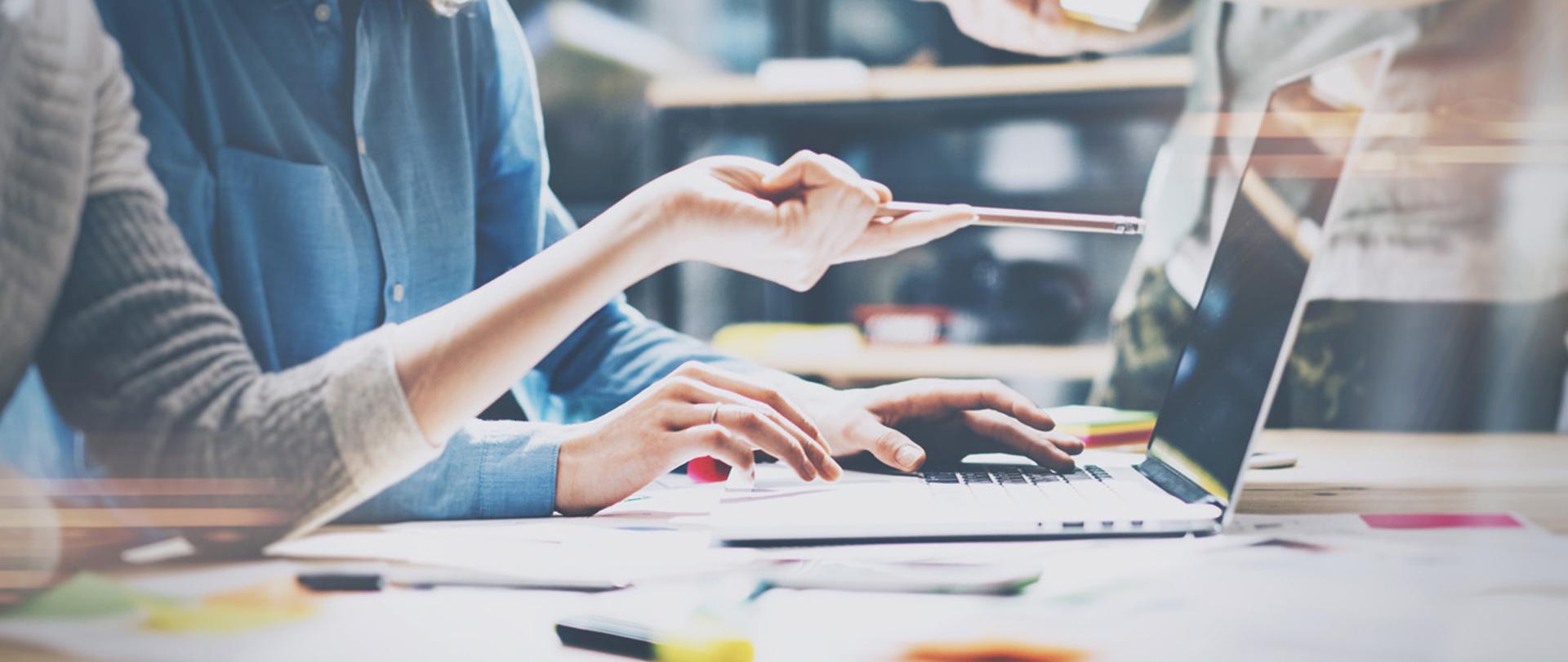 ręka z ołówkiem wskazująca na otwarty laptop