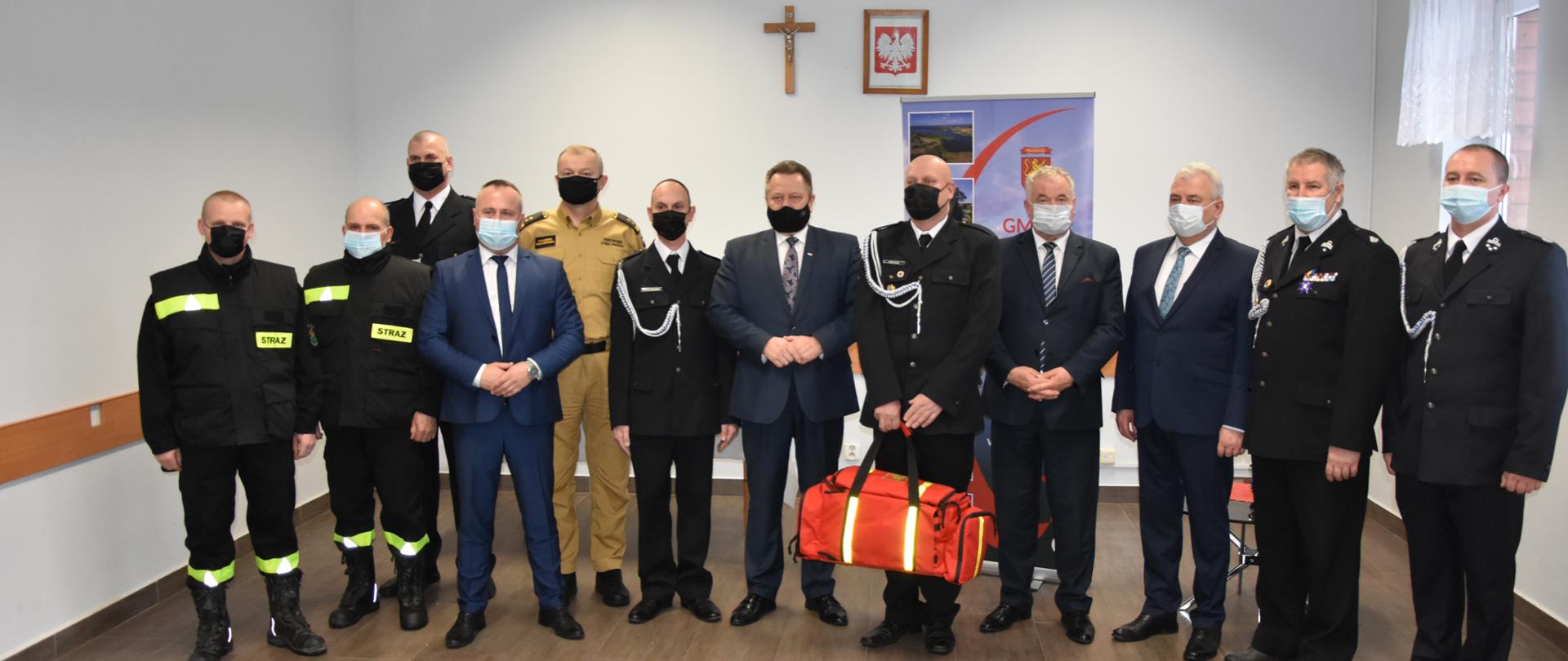 Zdjęcie obrazuje posła na sejm RP, samorządowców powiatu suwalskiego, strażaka PSP i druhów OSP a jeden z nich trzyma torbę medyczną
