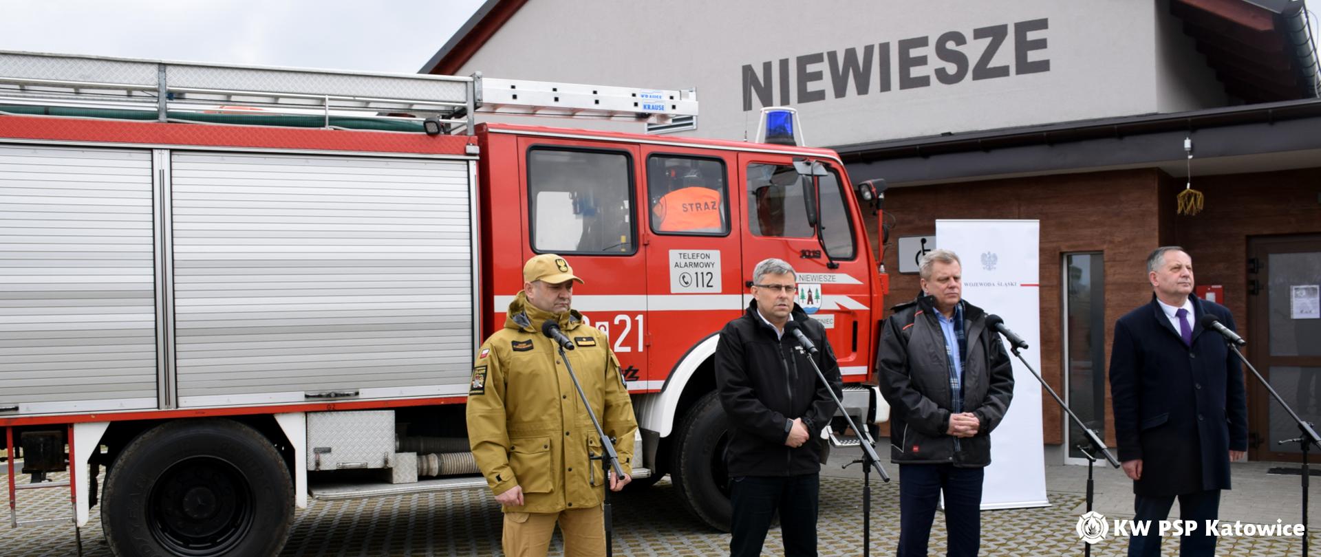 Od lewej przy mikrofonach: Śląski Komendant Wojewódzki PSP nadbryg. Jacek Kleszczewski, Wojewoda Śląski Jarosław Wieczorek oraz dwóch pozostałych uczestników konferencji, w tle samochód ratowniczo-gaśniczy oraz budynek komendy OSP w Niewieszach 