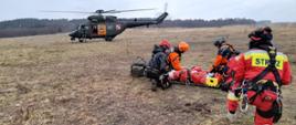 Zdjęcie przedstawia śmigłowiec oraz strażaków niosących poszkodowanego do niego.