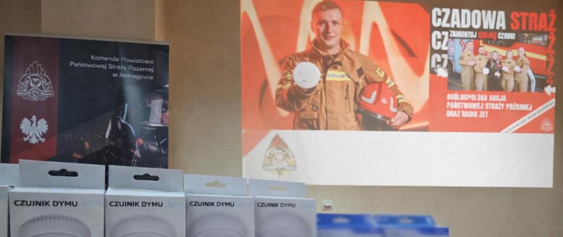 Na zdjęciu czujki tlenku węgla oraz dymu. W tle prezentacja pod tytułem „Czadowa Straż”.