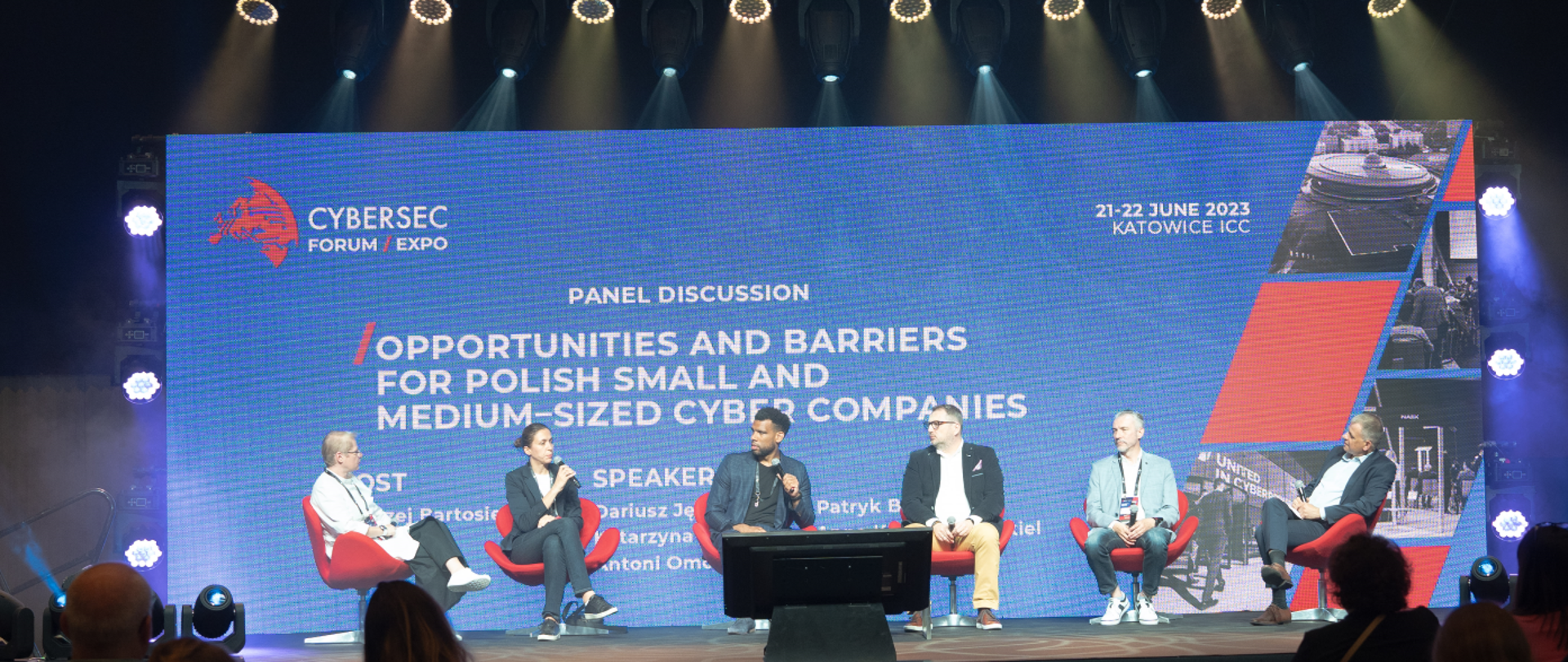 dyskusja panelowa sześć osób na czerwonych fotelach z mikrofonami