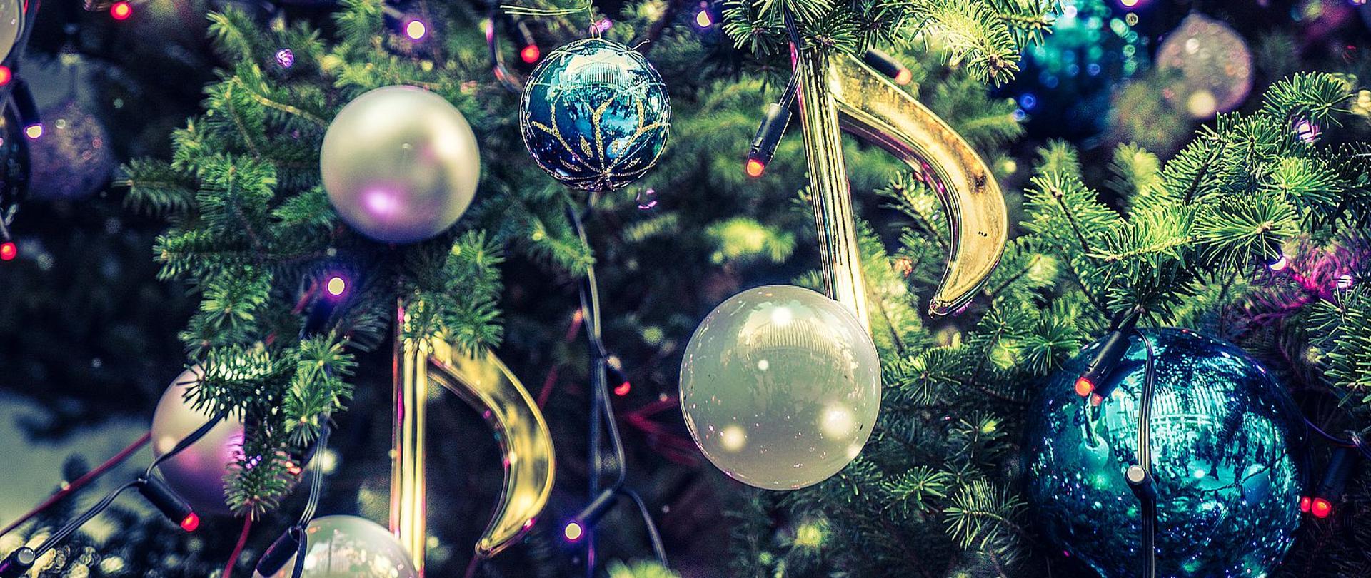 Zdjęcie przedstawia bombki w kształcie nut zawieszone z kolorowymi lampkami na choince.