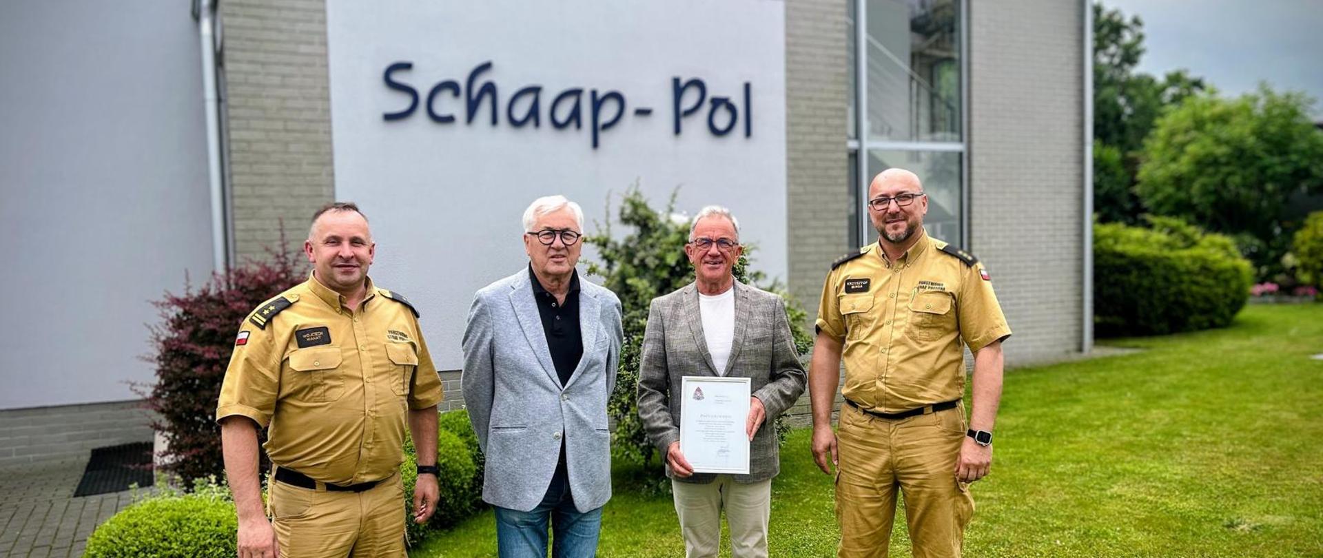 Na zdjęciu Komendanci Powiatowi PSP w Pucku bryg. Wojciech Wanat i kpt. Krzysztof Minga oraz przedstawiciele firmy Schaap Pol. Funkcjonariusze są są ubrani w stroje służbowe w kolorze piaskowym. Na drugim planie budynek firmy Schaap Pol. 