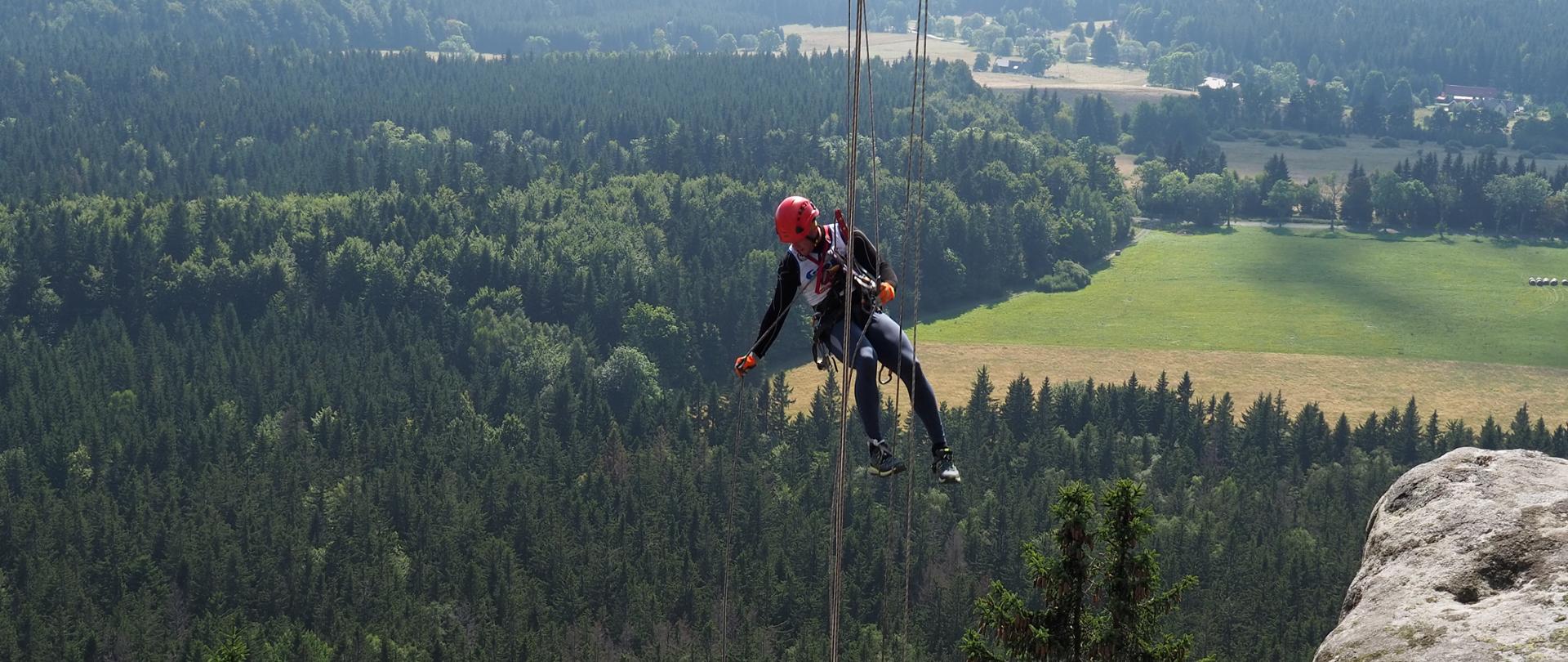 Strażak zjeżdżający na linie, w tle pasmo górskie. 