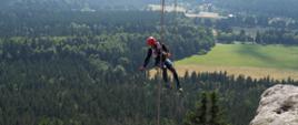 Strażak zjeżdżający na linie, w tle pasmo górskie. 