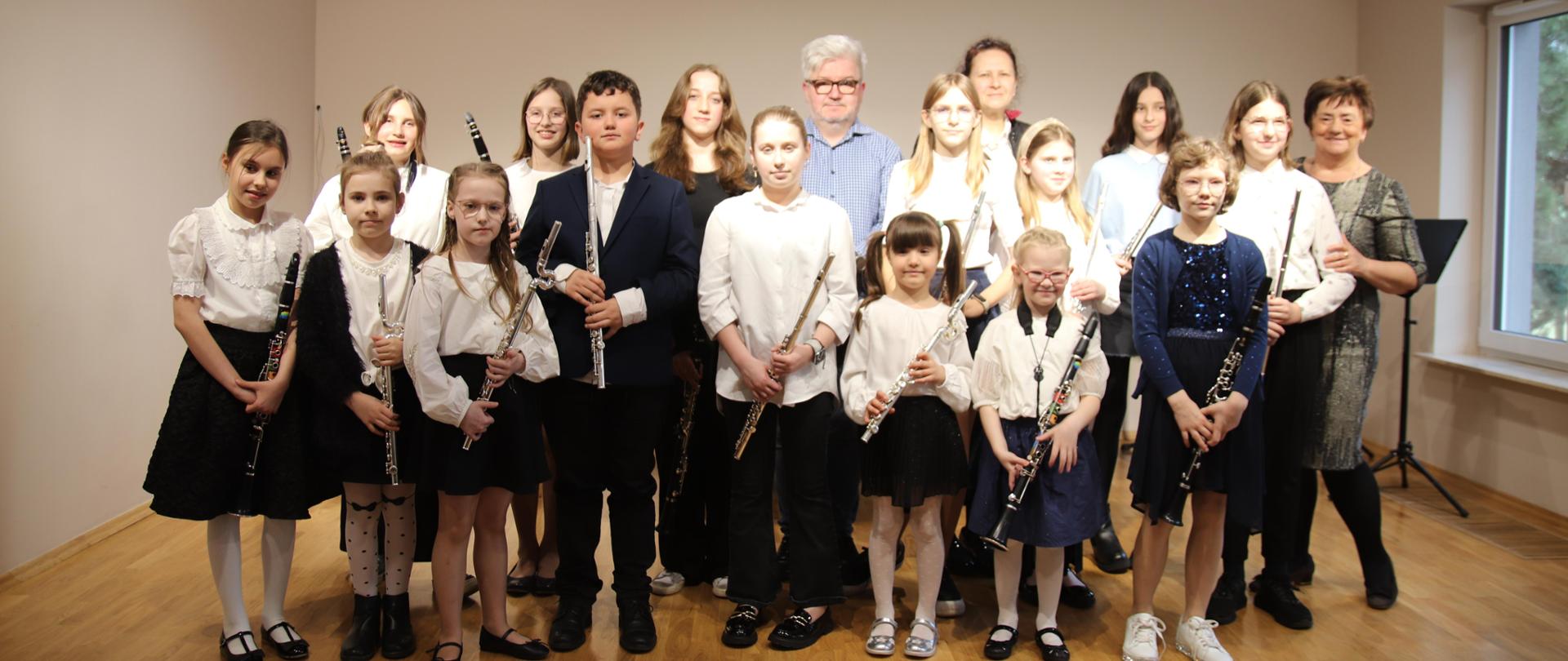 Grupa uczniów stoi z instrumentami w rękach na scenie sali koncertowej