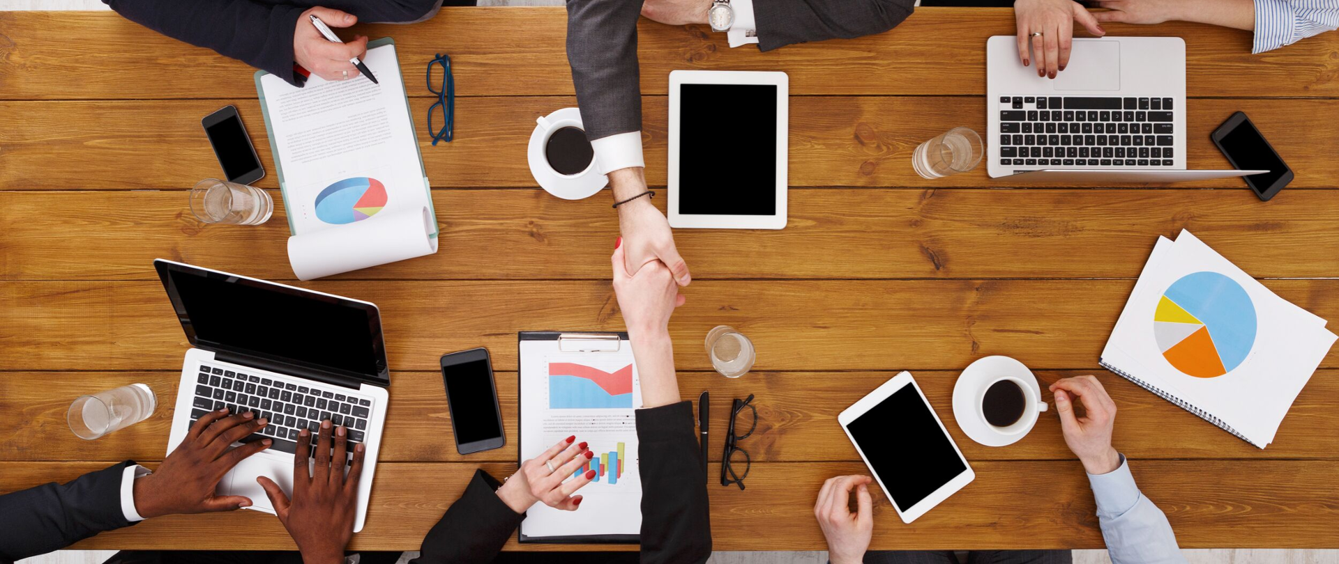 Sześć osób siedzi przy stole, widok z góry, dwie z nich podają sobie dłonie.