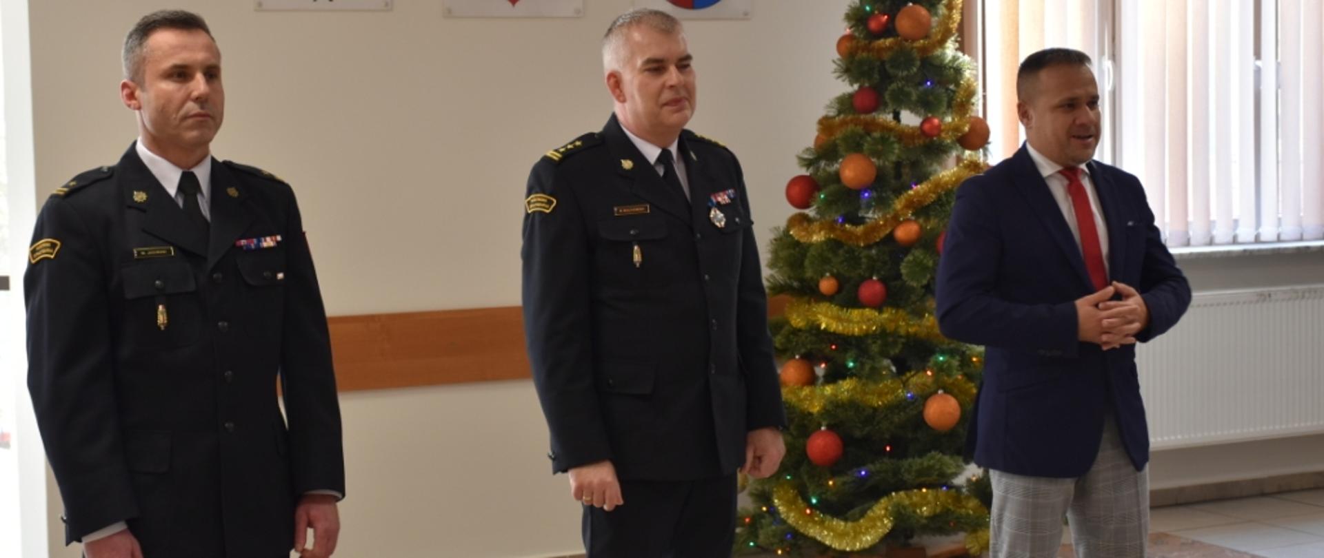 Zdjęcie obrazuje p.o. Zastępcę Świętokrzyskiego Komendanta Wojewódzkiego PSP w Kielcach st. bryg. Marcina Machowskiego, Starostę Powiatu skarżyskiego pan Artura Berusa, p. o. Komendanta Powiatowego PSP w Skarżysku-Kamiennej mł. bryg. Marcina Jasińskiego. Wszyscy biorą udział w spotkaniu opłatkowym w KP PSP w Skarżysku-Kamiennej.