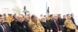 Zaproszeni goście oraz strażacy siedzą na krzesłach podczas narady.