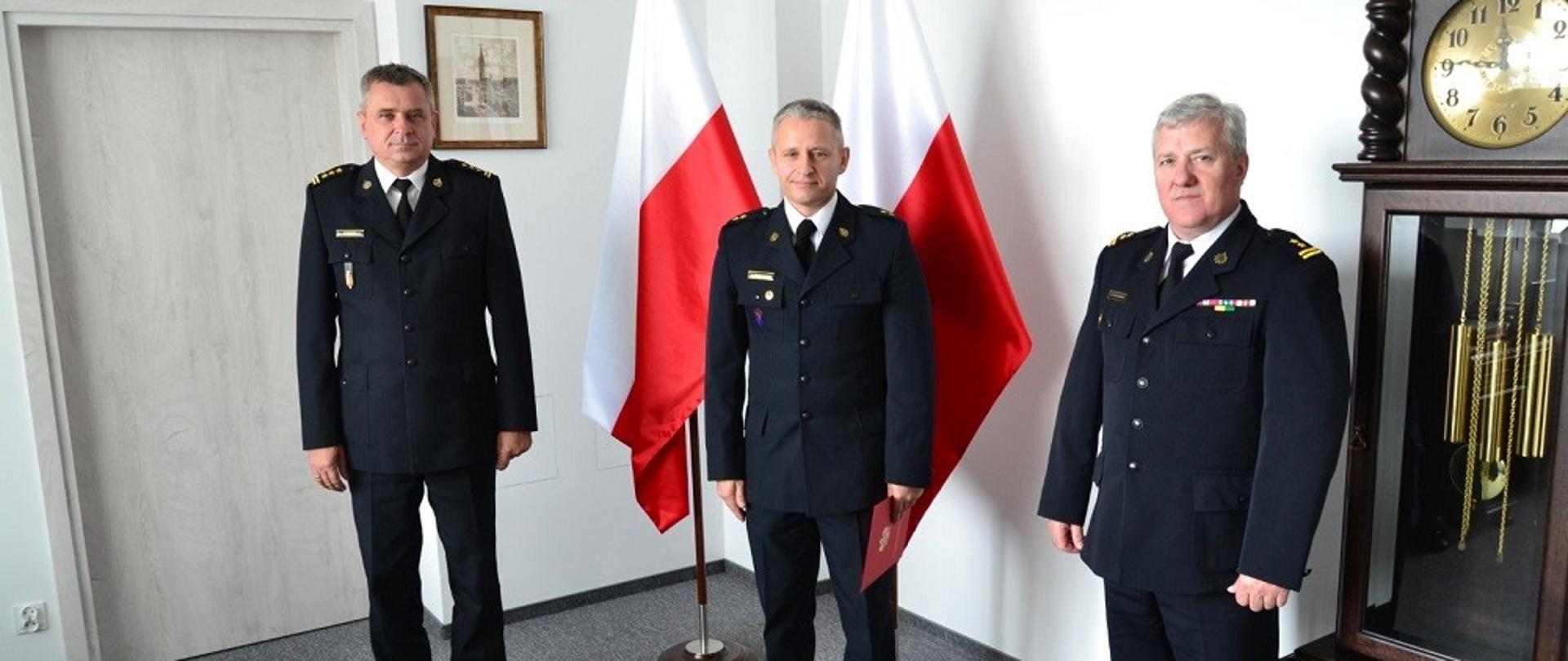 Od lewej Pomorski Komendant Wojewódzki, w środku na tle flag państwowych Hubert Grzesiowski, po prawej Janusz Leszczewski.