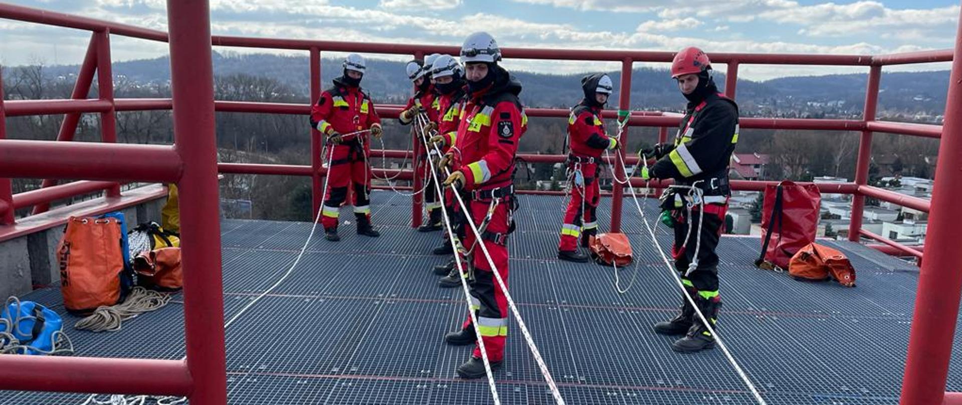 Siedmiu strażaków na wieży wysokościowej w trakcie szkolenia z ratownictwa wysokościowego. 