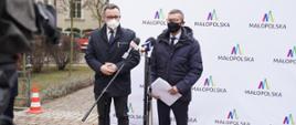 Wiceminister rozwoju, pracy i technologii Robert Tomanek i wicemarszałek Małopolski Tomasz Urynowicz stojący przy mikrofonach, za ich plecami baner z napisami "Małopolska"