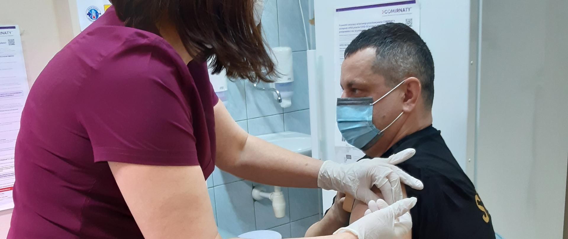 strażak w gabinecie lekarskim szczepiony w lewą rękę