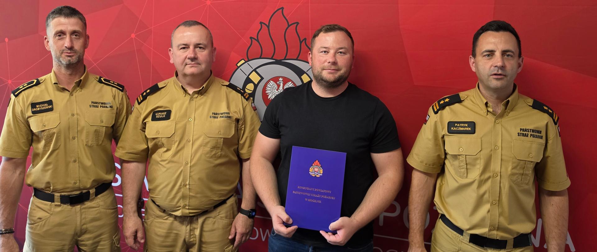 Przedstawiciel firmy, która wygrała przetarg na prace rozbiórkowe pod budowę nowej komendy wraz komendantem, zastępcą dowódcy JRG i głównym księgowym na tle baneru KP PSP Mogilno