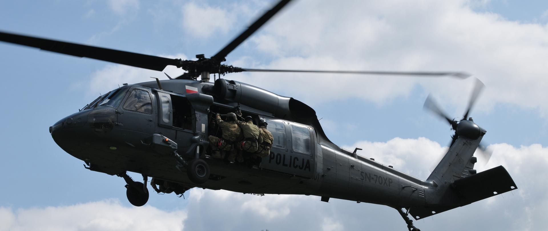 Na zdjęciu widoczny jest policyjny śmigłowiec oraz strażacy przygotowujący się do zjazdu po linie.