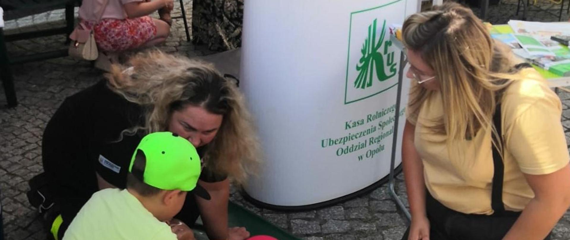 Dwie kobiety pokazują dzieciom na fantomie, jak uciskać klatkę piersiową.