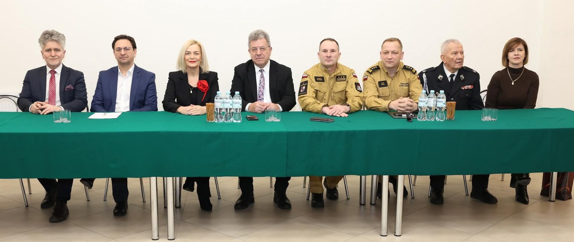 Zdjęcie przedstawia organizatorów i gości siedzący przy stole podczas spotkania sprawozdawczego Ochotniczej Straży Pożarnej.