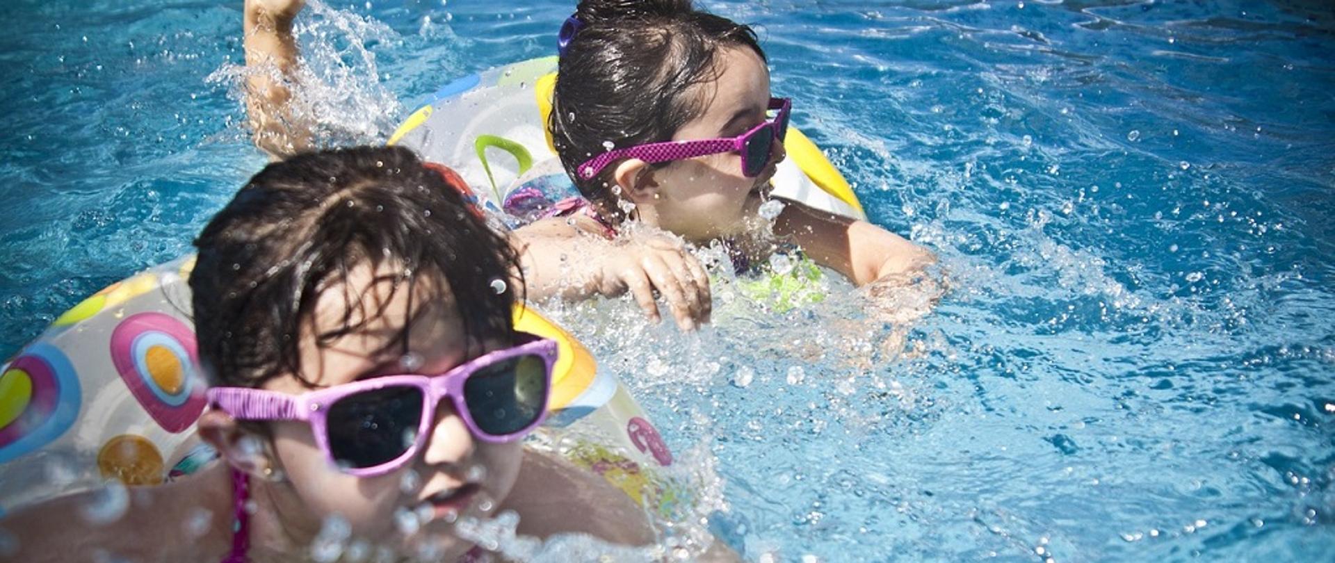 Dwie dziewczynki w okularach przeciwsłonecznych i w kółkach pływają w wodzie