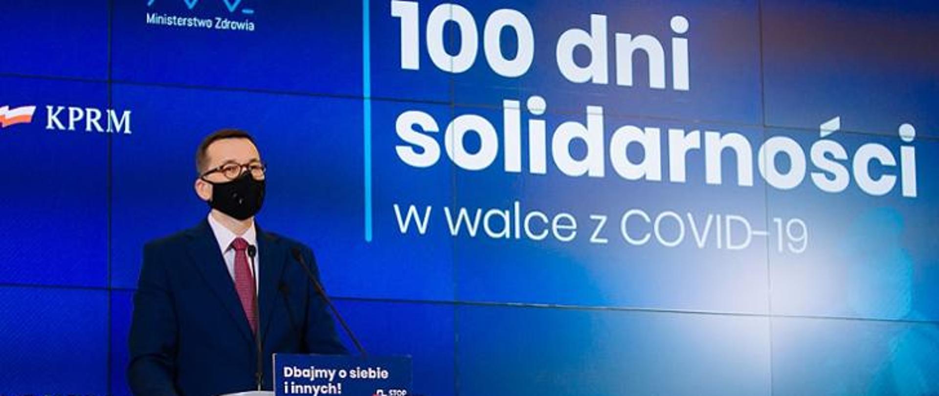 Premier Mateusz Morawiecki na tle ścianki wizyjnej z napisem: 100 dni solidarności w walce z COVID-19.