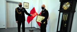 Zdjęcie przedstawia pomorskiego komendanta wojewódzkiego PSP st. bryg. Piotra Sochę wręczającego decyzję o odwołaniu ze stanowiska komendanta powiatowego PSP w związku z przejściem na zaopatrzenie emerytalne st. bryg. Grzegorza Kmiecika. 