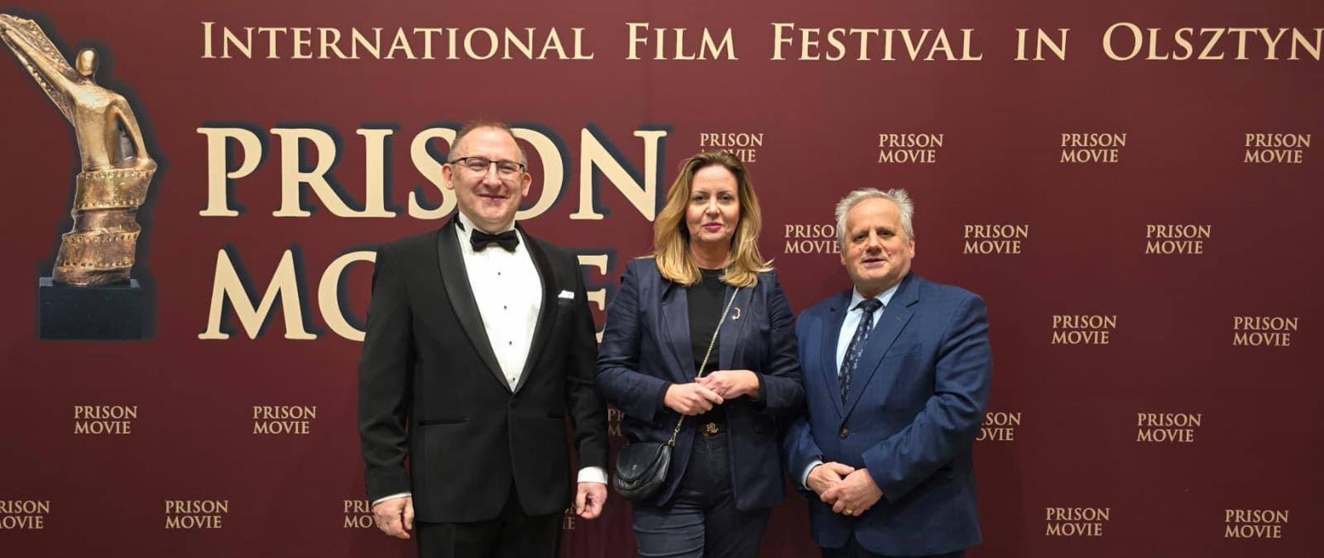 Trzy osoby stoją a za nimi znajduje się ścianka z napisem XIII International Film Festival „Prison Movie” 