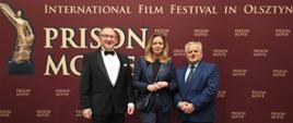 Trzy osoby stoją a za nimi znajduje się ścianka z napisem XIII International Film Festival „Prison Movie” 