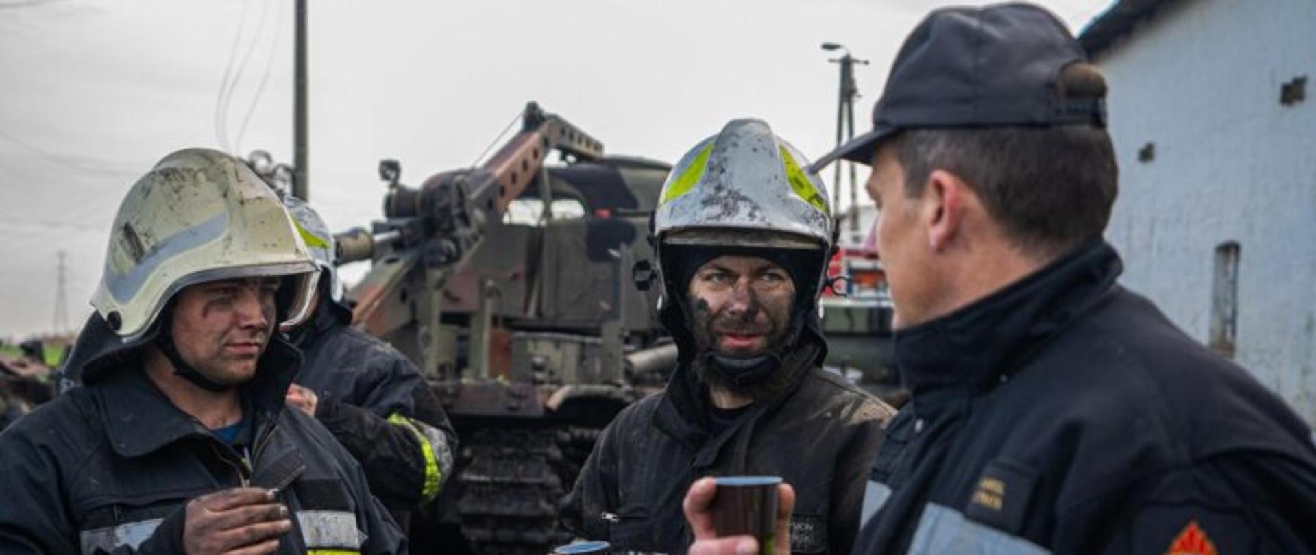 Na zdjęciu widać dwóch strażaków i Komendanta PSP Chełmno który pije kawę oraz rozmawia z druhami po pożarze w Raciniewie