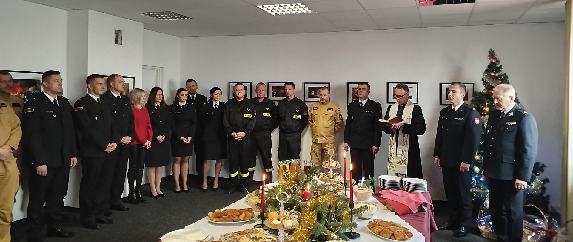 Na zdjęciu widoczni są: funkcjonariusze i pracownicy cywilni Komendy Powiatowej Państwowej Straży Pożarnej w Ostrowcu Świętokrzyski oraz Wiceprezes Zarządu Oddziału Wojewódzkiego Związku OSP RP, Wiceprezes Zarządu Oddziału Powiatowego Związku OSP RP, członkowie prezydium Zarządu Oddziału Powiatowego ZOSP RP oraz kapelan powiatowy strażaków podczas spotkania opłatkowego. 
