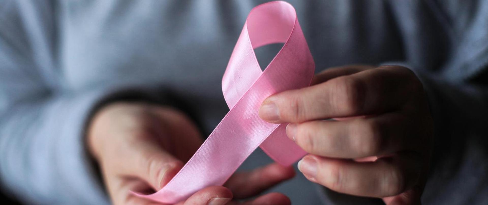 Kobieta trzyma w dłoniach różową wstążkę - symbol solidarności z osobami chorującymi na raka piersi 