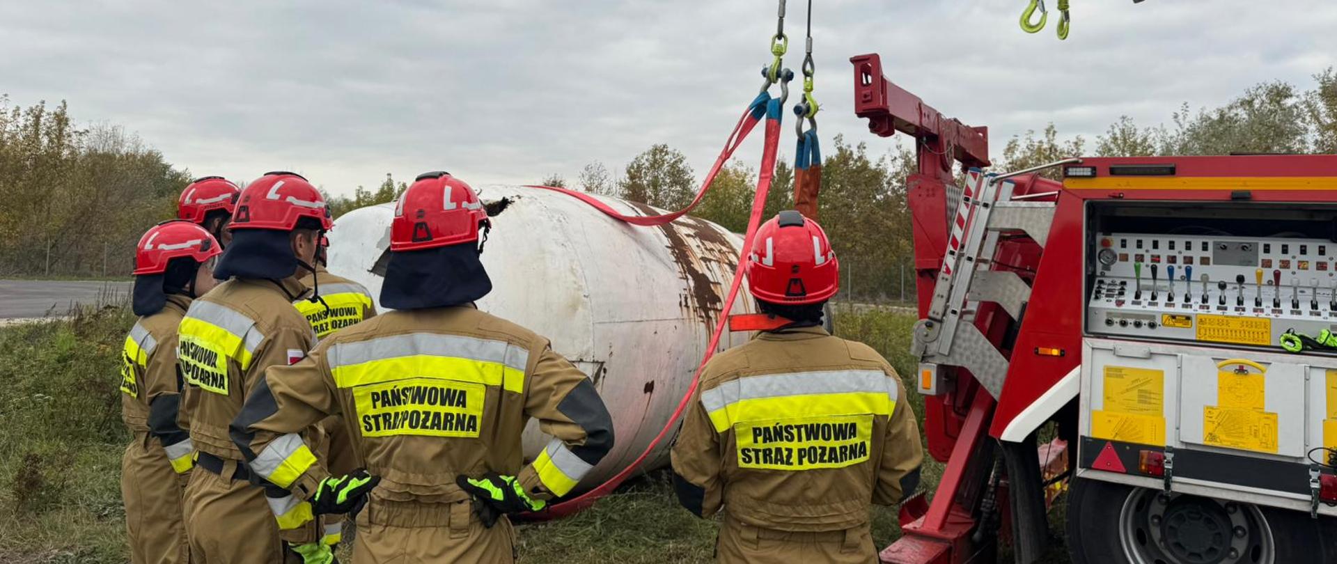 Zdjęcie przedstawia ratowników na tle podnoszonego przez samochód ratownictwa technicznego zbiornika betonowozu.
