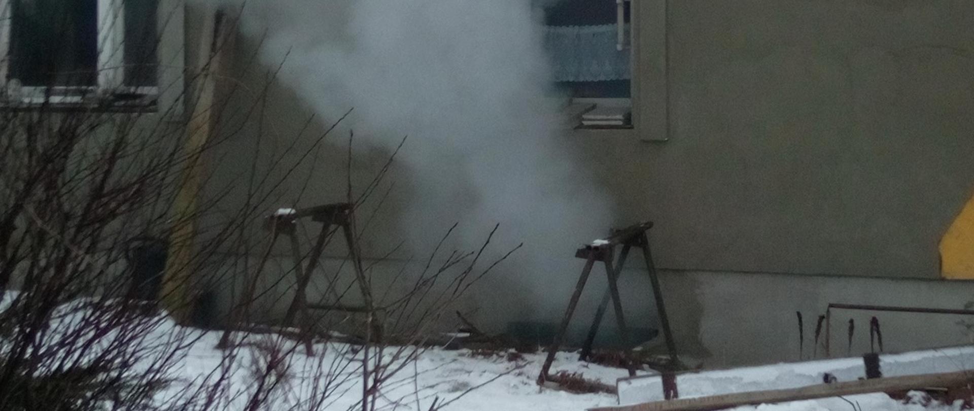 Na zdjęciu widać gęsty dym wydobywający się z okienka piwnicznego z pomieszczenia, w którym wybuchł pożar