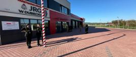 Zdjęcie przedstawia poczet flagowy oraz strażaków podczas uroczystej zmiany służby wraz z podniesienie flagi państwowej na maszt