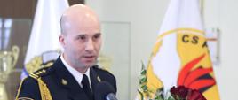 Zastępca Komendanta Centralnej Szkoły PSP w trakcie przemowy. W dłoni trzyma bukiet czerwonych róż