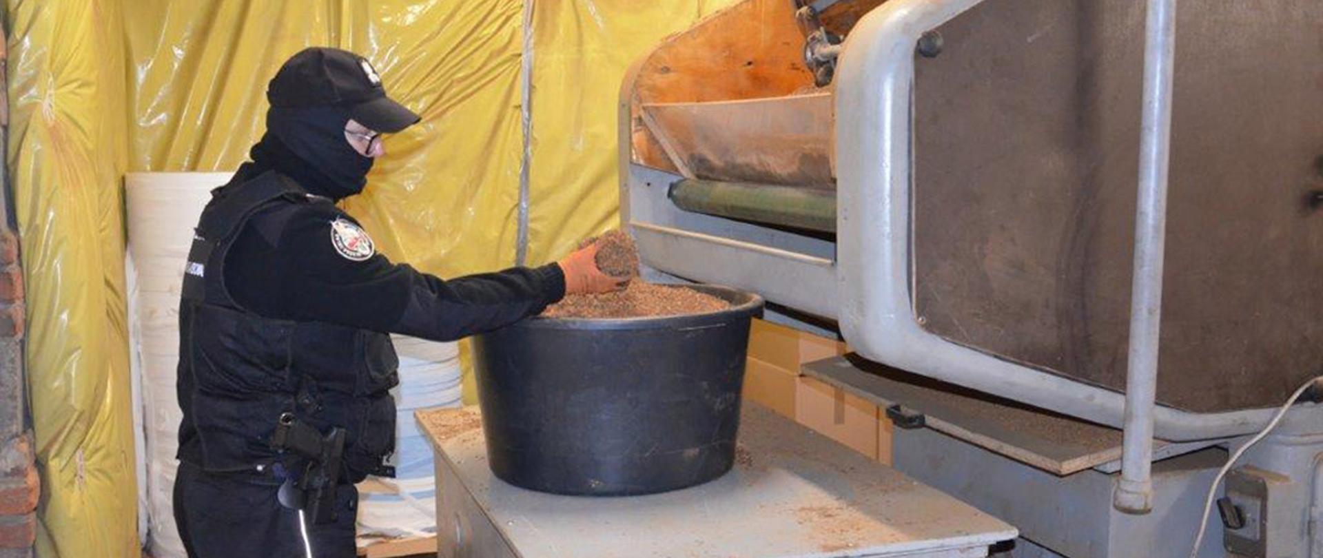 Funkcjonariusz Służby Celno-Skarbowej przy maszynie do nielegalnej produkcji papierosów.