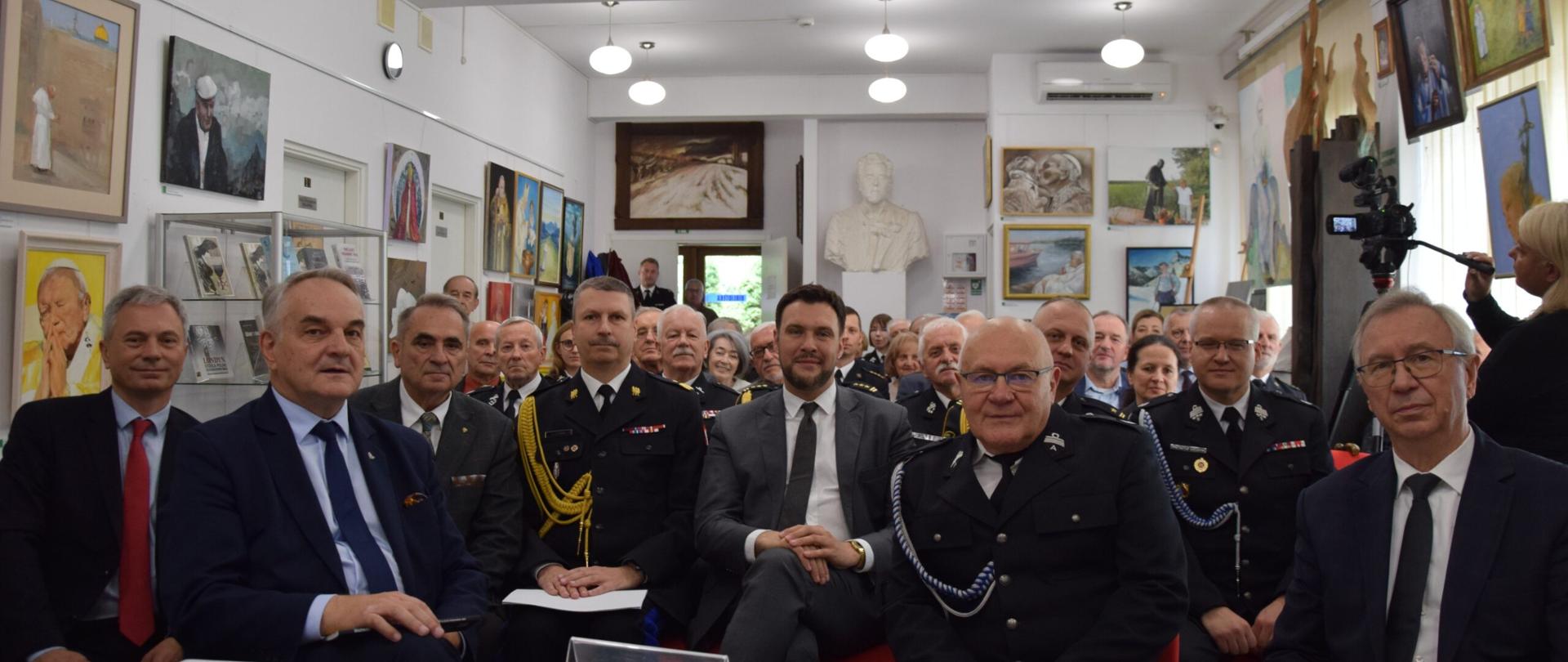 Warszawa, 1 października 2025 roku – uczestnicy uroczystego spotkania w Muzeum Historii Polskiego Ruchu Ludowego z okazji 104. rocznicy zjednoczenia ruchu strażackiego oraz promocji drugiego tomu Słownika biograficznego polskich strażaków. W pierwszym rzędzie widoczni przedstawiciele władz państwowych, Związku Ochotniczych Straży Pożarnych RP oraz oficerowie straży pożarnej. W tle zgromadzeni goście i dekoracje artystyczne muzeum.