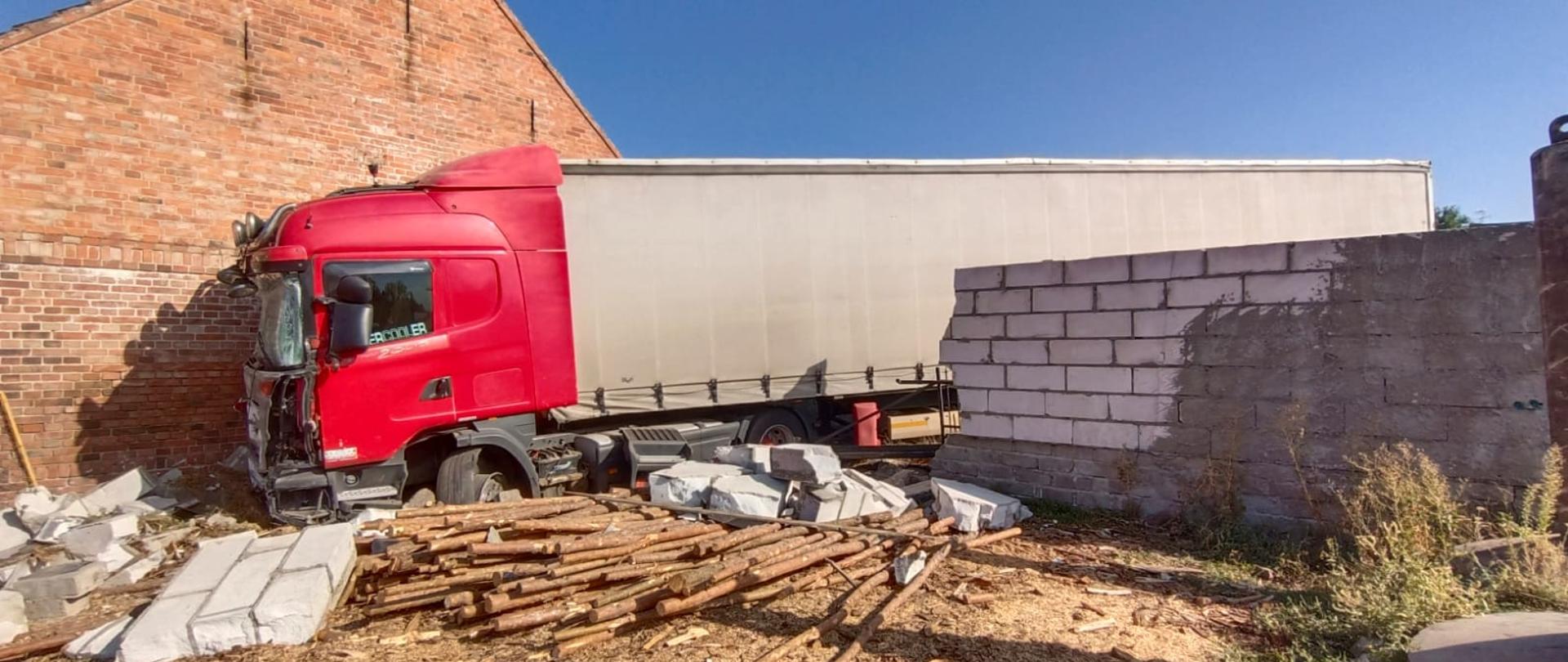 Widać uszkodzone betonowe ogrodzenie, samochód ciężarowy jest przy budynku