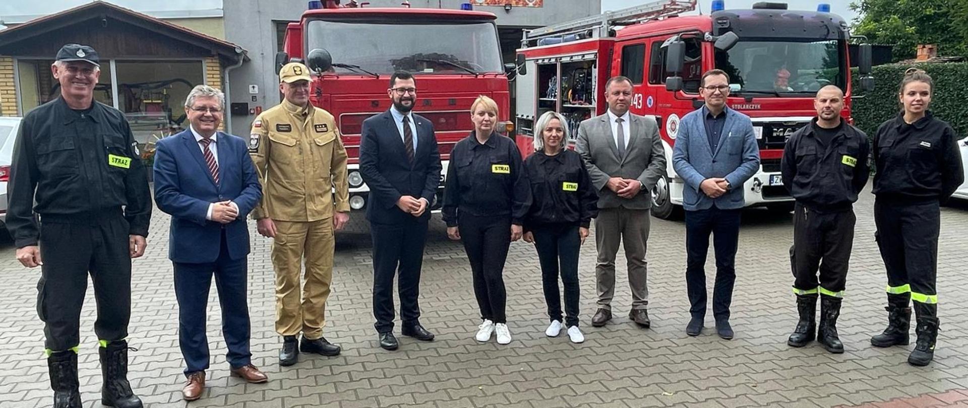 Spotkanie w OSP Dębołeka, na pierwszym planie uczestnicy spotkania, min. Zachodniopomorski Komendant Wojewódzki PSP Jarosław Tomczyk. W tle pojazdy druhów OSP oraz remiza strażacka.