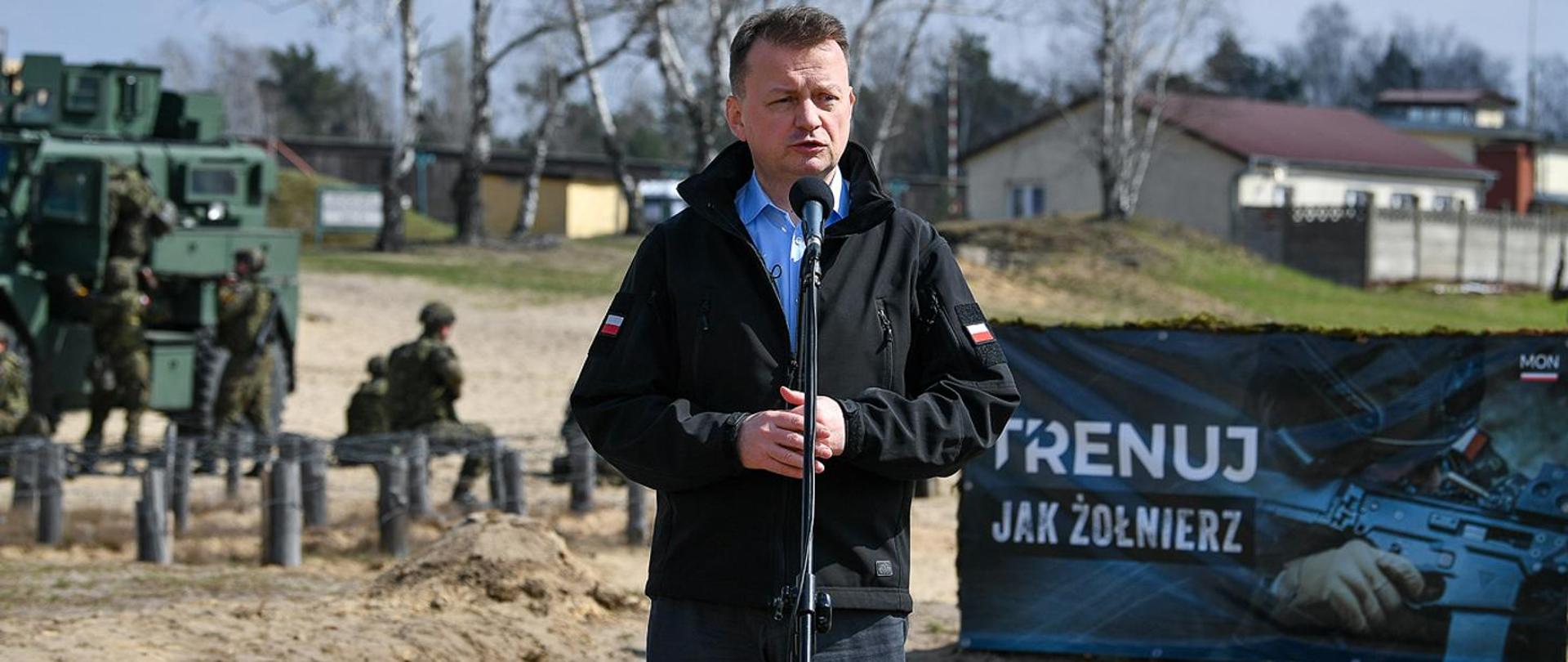 Zdjęcie ministra obrony Mariusz Błaszczak mówiącego do mikrofonu na poligonie 