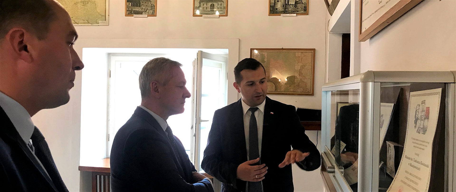 Trzech mężczyzn ogląda wystawę. W środku minister Marek Zagórski