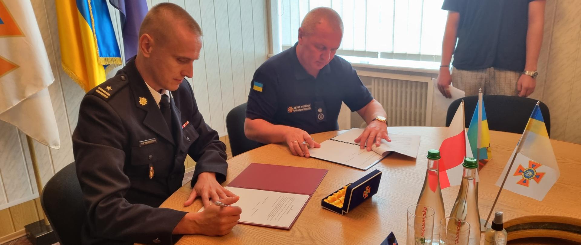 Dwóch strażaków siedzących przy stole i podpisujących porozumienie 