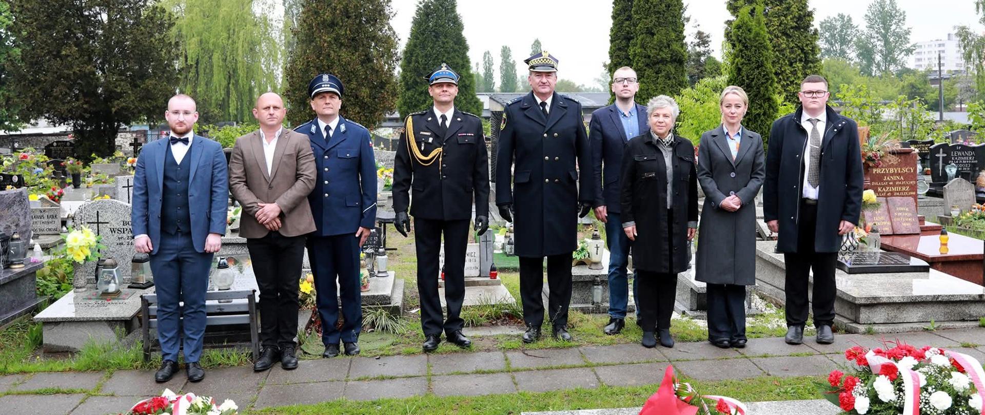 Na cmentarzu przy ul. Smutnej w Sosnowcu grupa uczestników uroczystości upamiętniających 80. rocznicę zakończenia II wojny światowej pozuje do wspólnego zdjęcia przy grobach wojennych. Wśród obecnych znajdują się przedstawiciele samorządu oraz służb mundurowych, w tym funkcjonariusz Państwowej Straży Pożarnej w umundurowaniu galowym. Na pierwszym planie widoczne są biało-czerwone wiązanki kwiatów złożone ku pamięci ofiar wojny.