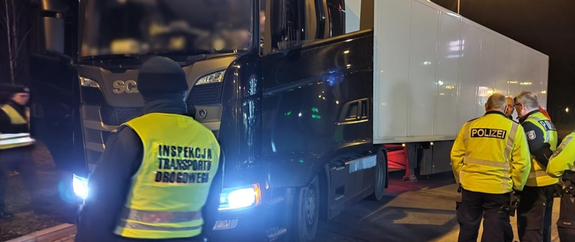Od lewej: umundurowani inspektorzy lubuskiej Inspekcji Transportu Drogowego i niemieccy policjanci z Brandenburgii stoją obok zatrzymanego do kontroli ciągnika siodłowego z podpiętą naczepą. 