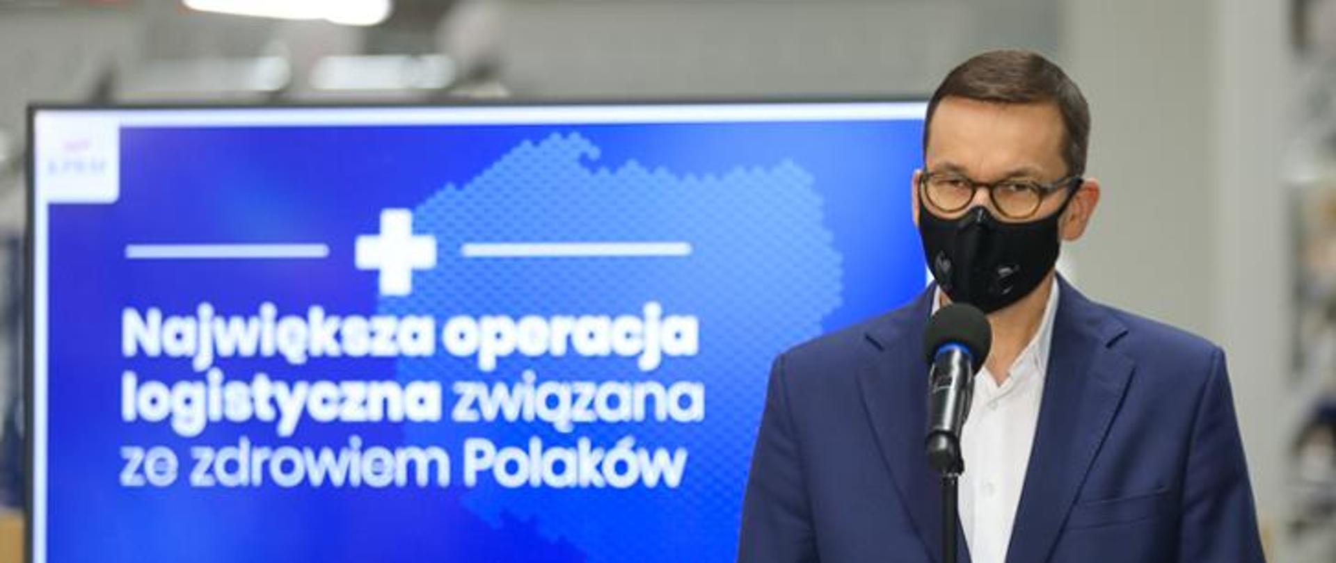 Premier Mateusz Morawiecki, w tle baner z napisem: Największa operacja logistyczna związana ze zdrowiem Polaków.